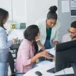 Tim beragam sedang berdiskusi aktif di kantor modern, menggambarkan program trainee atau management trainee di perusahaan